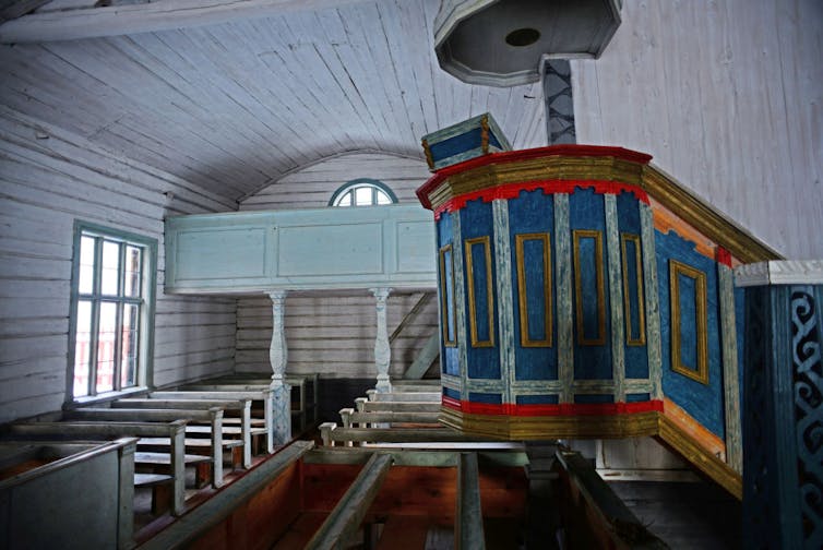Scandinavia has its own dark history of assimilating Indigenous people, and churches played a role – but are apologizing The sanctuary of an old church, painted in white and light blue, with a more brightly colored pulpit.