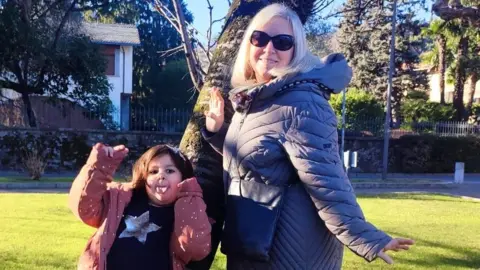 Summer holiday clubs now cost an average of £1,076 per child Chiara Del Vescovo Chiara Del Vescovo and her daughter hold their arms out as they pose next to a tree in a park
