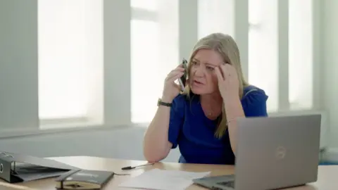 Imported dogs 'posing risk to UK', RSPCA warns Kath Stanczyszyn in a blue top on a phone sitting in an office. There is a desk in front of her, with a laptop to her left and windows behind her
