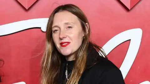 Crying at work - career damaging or just human? Getty Images Amy Powney, dressed in black, with long brown hair and red lipstick, stands in front of a red background