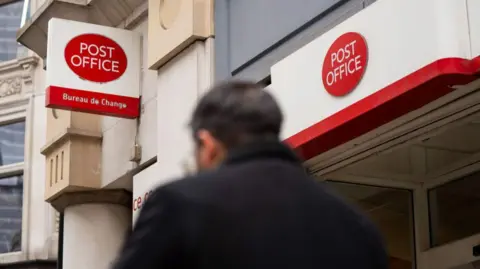 Post Office could be owned by its workers, government says Getty Images Man in dark jacket with dark hair walks past Post Office branch