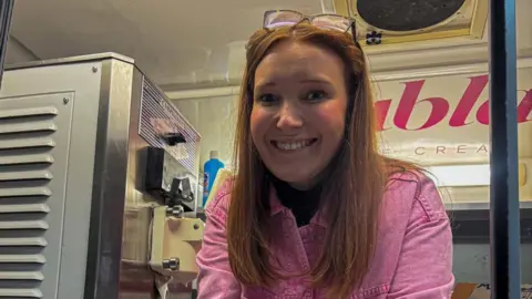 Porthcawl Coney Beach fair to close in October after 100 years Lauren Evans leaning out of ice cream shop window wearing a pink shirt. She has red long hair and glasses pushed up into her hair