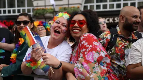 London Pride returns as events struggle with falling funds Getty Images A picture focused on two attendees of a previous Pride in London event. On the left, a woman with glitter on her face and with flowery decorations around her head and arms laughs at the camera. On the right, another woman smiles at the camera with red-heart sunglasses on and a red flowery dress.