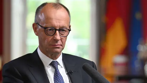 Jeff Overs/BBC Germany's chancellor sits in a dark jacket and tie 