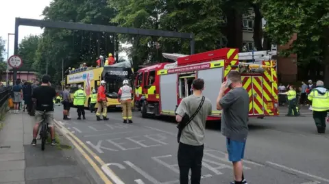 Fifteen hurt as double-decker bus hits bridge Tyler Tyldesley People stand around looking at a fire truck which is parked in front of a yellow double decker bus which has had its top ripped off and the top windscreen smashed. Firefighters in helmets and high vis are standing on the exposed top deck.
