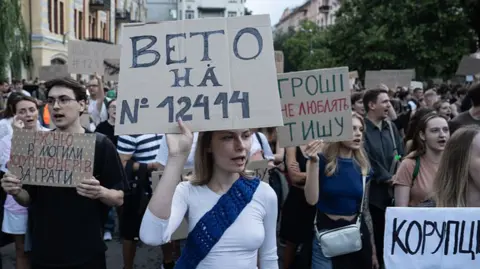 Ukraine backlash grows after Zelensky strips anti-corruption bodies of independence Getty Images Young Ukrainians in Kyiv hold placards, including a young woman with a white T-shirt and a blue sash