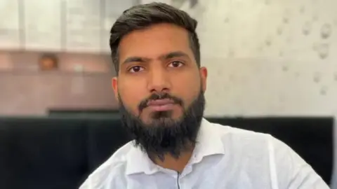 Victim's relative 'can't be at peace' until root cause known A man wears a white dress shirt and has a microphone attached to his lapel. He has a black beard and dark hair.