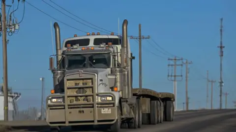 Trucking's uneasy relationship with new tech Getty Images A truck drives along a backroad, with electric poles and wires stretching across the landscape in Edmonton, Alberta