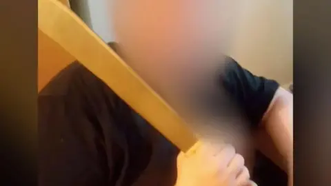 How MI5 piled falsehood on falsehood in court in the case of a spy who abused women A heavily blurred photo of X, who is wearing a black T-shirt and holding a large machete