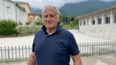 'The village will die' - Italy looks for answers to decline in number of babies Mayor Giacomo de Luca, a man in a navy blue polo shirt, stands in front of buildings