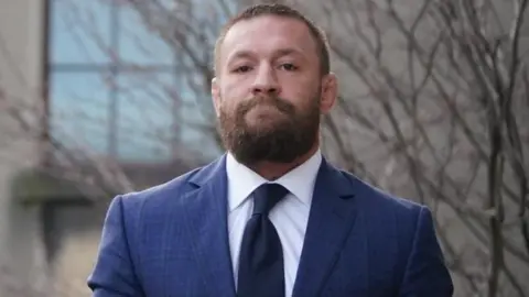 MMA fighter loses appeal in civil rape case PA Media McGregor is wearing a navy suit with a white shirt and dark coloured tie. He has a thick brown beard and short brown hair. He has a straight face looking directly at the camera.