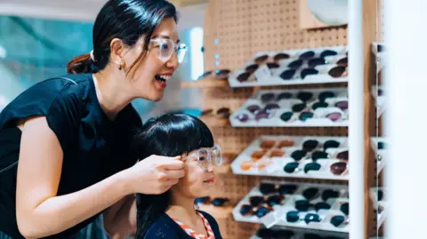 'Autofocus' specs promise sharp vision, near or far Getty Images A mother tries on glasses in a store with her young daughter