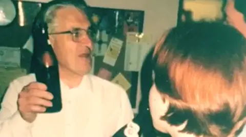 Police investigate sex abuse claims against men linked to Church A white man wearing glasses with black and white wavy hair and wearing a white shirt with a bottle of bear in his hand. In the foreground, is the back of the head of a ginger-haired girl