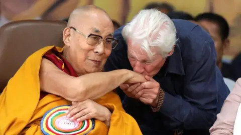 Thousands turn out to celebrate Dalai Lama's 90th birthday EPA/Shutterstock US actor Richard Gere, in a navy shirt and with wooden bracelets on, kisses the hand of the Dalai Lama cloaked in a yellow robe with a bright multi-coloured brooch on.