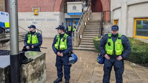 Epping council votes to urge government to shut asylum hotel Pete Walker/BBC Three police officers are stood outside Epping Forest District Council offices