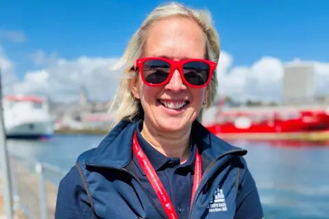 'Party city' event gets under sail Woman - Emma Wadee - with blonde hair and red-framed sunglasses with Aberdeen harbour in the background.