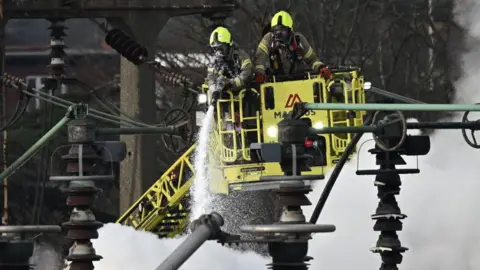 Five takeaways from report into fire that shut Heathrow down Getty Images Two fire fighters wearing breathing apparatus are on board a platform which has lifted them above the electrical substation which caught fire in March. One is holding a hose which is dampening down the flames. Smoke is billowing.