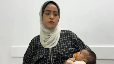 An image of Najah, a 19-year-old woman, holding a baby in her arms. 
