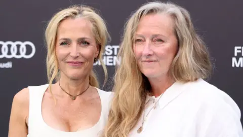 Author Raynor Winn defends herself against claims she misled readers Getty Images Gillian Anderson and Raynor Winn attend the premiere of the movie The Salt Path during the 2025 Munich Film Festival on 1 July. They are both wearing white tops.