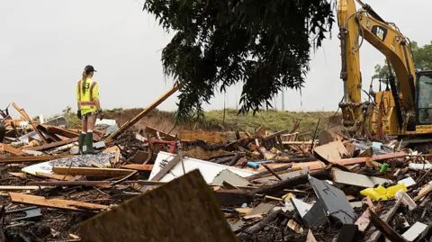 81 dead and dozens missing as more rain looms Getty Images Workers operate heavy machinery to clear debris after massive flooding