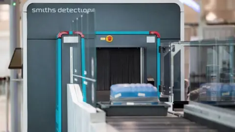Edinburgh Airport liquid limit increased from 100ml to two litres Smiths Detection A Smiths Detection airport security scanner with a blue suitcase in a tray on the conveyor belt.