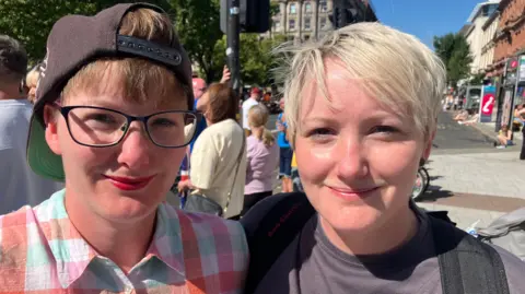 Thousands attending NI's Orange Order parades Melissa and Lyndsay smiling in the sun. Melissa has a hat on and glasses.