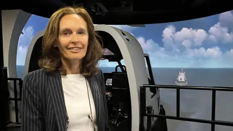 Defence firms 'confident' hundreds more jobs will come A woman in a pin stripe blue jacket and a white top, smiles at camera. There is a flight simulator behind her.