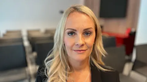 Military aircrew pursuing MoD after cancer diagnoses reaches 180 Louisa Donaghy is sitting in an office. She has long blonde wavy hair and is wearing a black blazer.