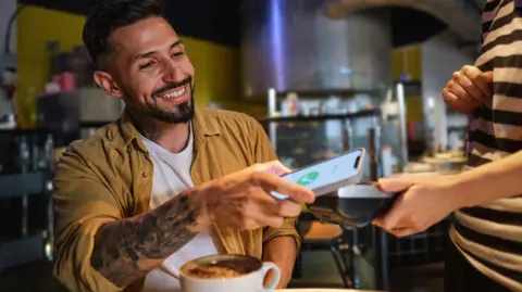 Your new banknote ideas - from British Bulldogs to Fawlty Towers Getty Images Smiling young man in a cafe pays using a phone with a coffee in front of him.