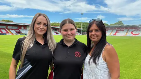 Household energy bills fall but may not go much lower Hannah Marsh, Gracie and Nadina Hill stand on the pitch at Stevenage Football Club with stands in the background