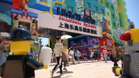 China bets on Western theme parks to lift spending Getty Images Dozens of visitors stream into Legoland Shanghai through an entrance at the base of a colourful hotel. In the photo is a large banner displaying the words "Legoland Shanghai Resort". Large mascots, based on Lego minifigurines, are pictured at the foreground of the shot.