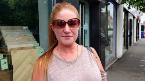 Food prices remain 'stubbornly high' in Northern Ireland as inflation rate rises A woman is standing on the street. She has long red hair tied in a pony tail and is wearing sunglasses. She's wearing a gold bar necklace.