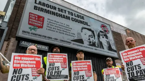 Unite votes to suspend Rayner's membership over bin strikes Getty Images Striking bin workers stand in front of billboards commissioned by the Unite trade union, holding placards in support of striking bin workers