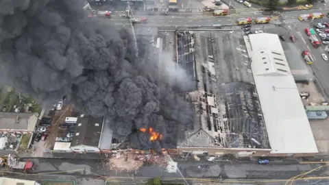 Homes evacuated as factories and tyres burn near Tipton West Midlands Fire Service An aerial shot of a factory fire with large amounts of grey smoke