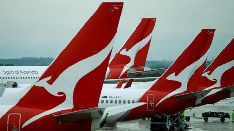 Qantas data breach to impact 6 million airline customers Reuters Four planes are lined up in a row on the tarmac of an aiport, each with the Qantas logo of a stylized white kangaroo on a red background emblazoned on the tail.