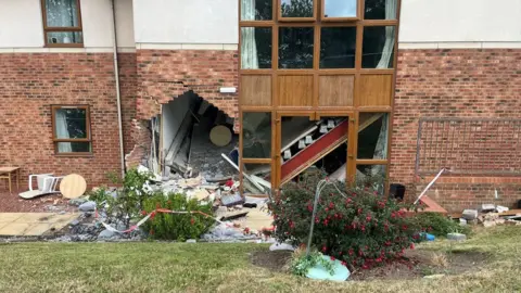 Arrests as Sunderland care home crash puts eight in hospital A large hole at the bottom left of a brick and white stone building next to a window. Bricks and debris from the wall are scattered all around and in the bushes and grass in front of the building.
