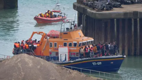 Small boats crossings hit 25,000 for the year PA Media A group of people thought to be migrants are brought in to the Border Force compound in Dover, Kent, from two Broder Force vessels following a small boat incident in the Channel.