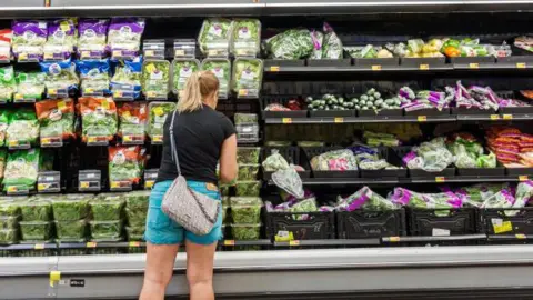 What have tariffs really done to the US economy? Getty Images Woman wearing a black T-shirt and blue shorts shopping in the fresh fruit and vegetable section of a US supermarket