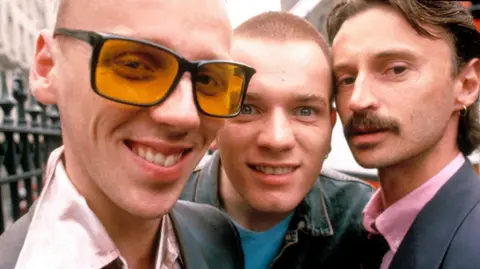 Trainspotting author Irvine Welsh says AI has made us dumbed down machines Shutterstock Close up shot from Trainspotting film showing Spud in sunglasses, smiling with pink shirt (Ewen Bremner), Renton sneering in blue T shirt (Ewan McGregor) & Begbie with earring and moustache in bright pink shirt (Robert Carlyle)
