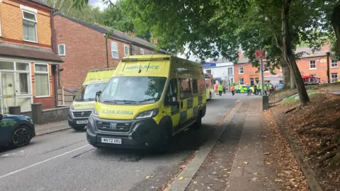 Fifteen hurt as double-decker bus hits bridge Richard Stead/BBC Two yellow ambulances are parked in the middle of a street. People can be seen walking along the street in the background.