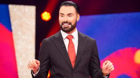 Which stars are missing, and why? Rylan Clark on stage presenting Comic Relief 2025
