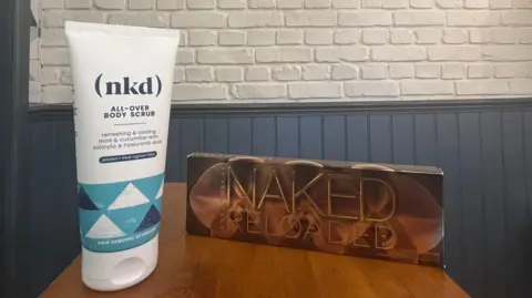 Salon owner 'ready' for key L'Oréal trademark dispute hearing A white tube which says (nkd) all over body scrub on a shelf next to an eye shadow pallet which says Naked Reloaded.