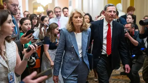 Senate Republicans narrowly pass Trump's 'big, beautiful' spending bill Getty Images Lisa Murkowski wears a blue jacket and white shirt walking through a crowd of people in the Capitol