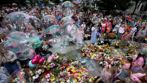 Southport attack 'one of the most egregious crimes' inquiry hears PA Media A crowd of people dressed in bright colours blow bubbles into the air over floral tributes. A group of young girls in pink tops stand to one side of the flowers