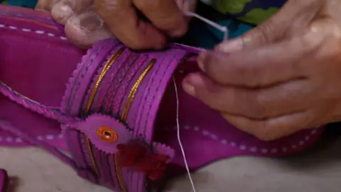 Why Indian footwear artisans are upset with the luxury Italian label A women threads a needle through a leather Kolhapuri slipper in a workshop in Kolhapur, Maharashtra