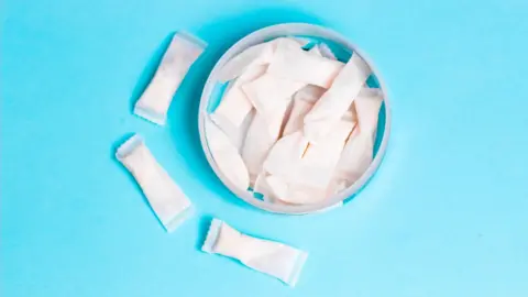 The rising use of nicotine pouches snus Getty Images Nicotine pouches are shown in a container, with some spilled beside it on a light blue background.