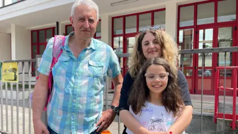 'The village will die' - Italy looks for answers to decline in number of babies An older man, a mum and a daughter are seen in front of a building