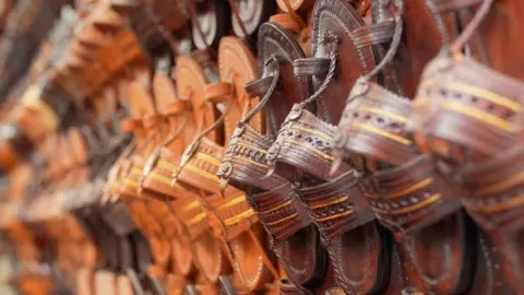Why Indian footwear artisans are upset with the luxury Italian label BBC The image shows Kolhapuri sandals in different shades of brown displayed at a shop.
