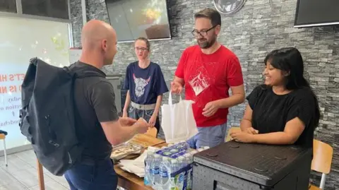Weston woman wins British Citizen Award for creating food bank Aishah Ahmed Aishah with volunteers at a table in her food bank. There are water bottles and food on the table and one of the volunteers is handing a man a plastic bag.