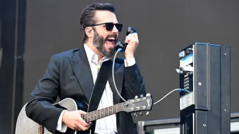 The 10-year-old song that keeps getting bigger Getty Images Ben Schneider singing into a payphone handset as a prop on stage, also holding a guitar